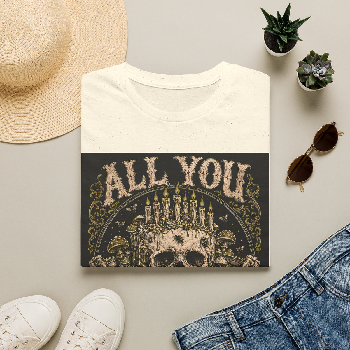 Folded cream t-shirt with All You Can Rot text and skull crowned with candles, styled flat lay.