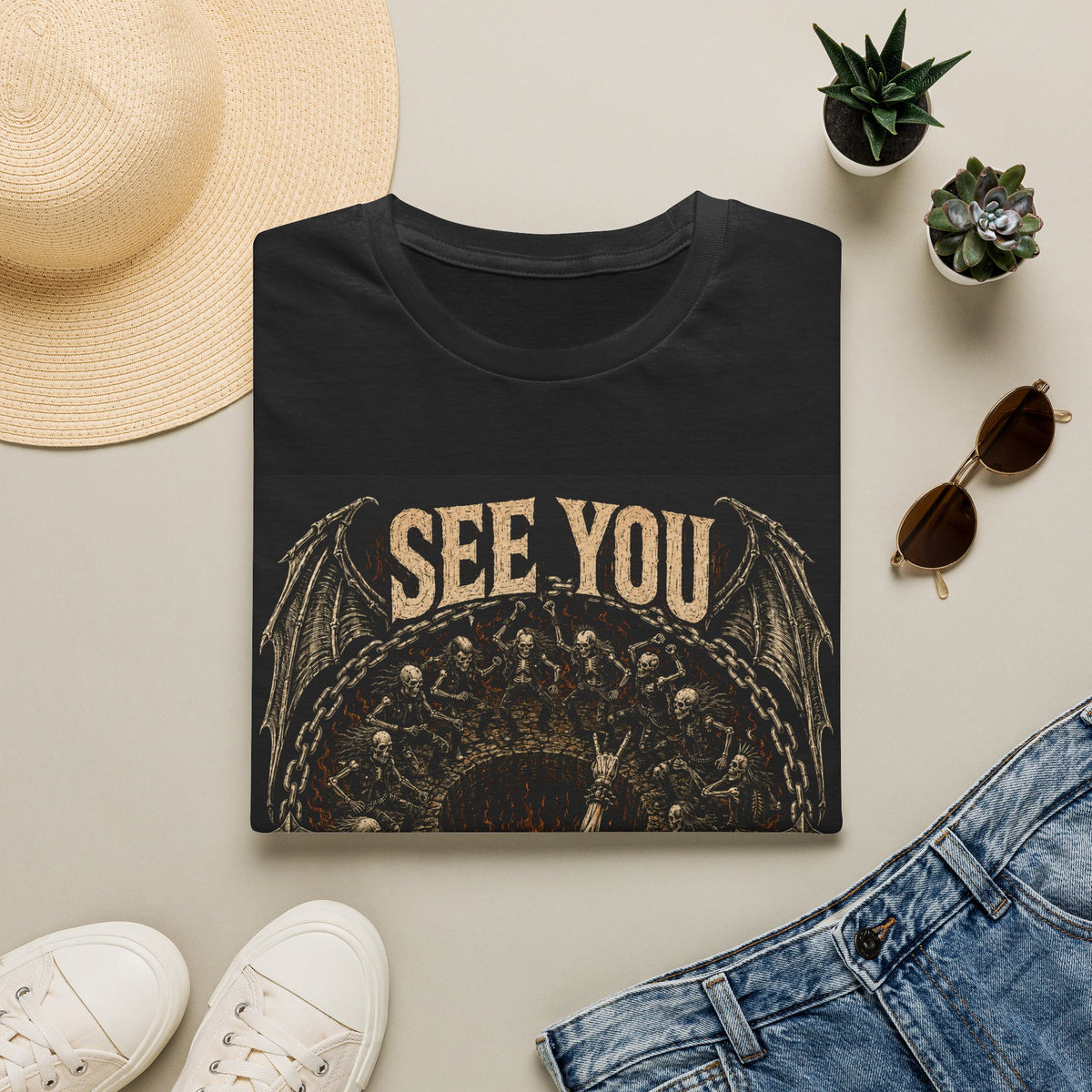 Folded black t-shirt with See You in the Pit text and ornate skull graphic, styled flat lay.