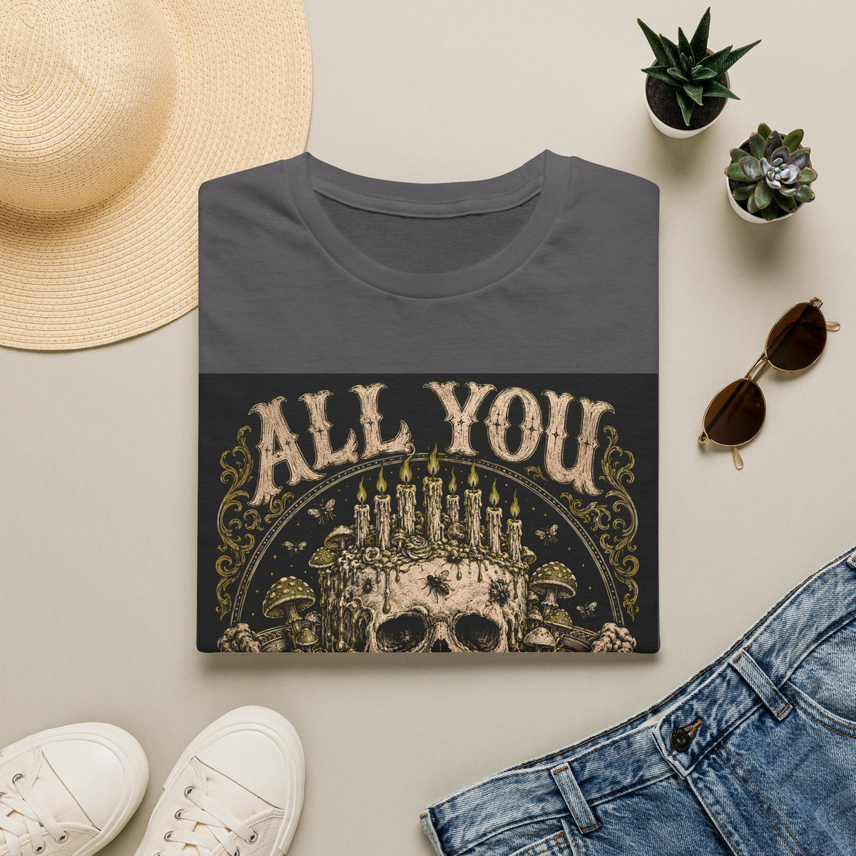 Folded charcoal grey t-shirt with All You Can Rot text and skull crowned with candles, styled flat lay.