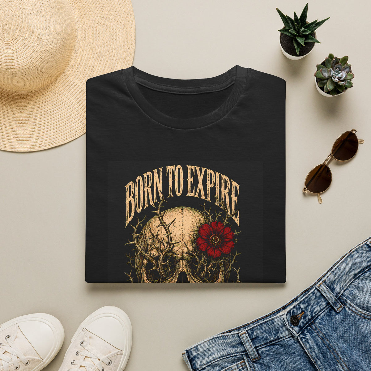 Folded black t-shirt with Born to Expire text with a skull and red flower, styled flat lay.